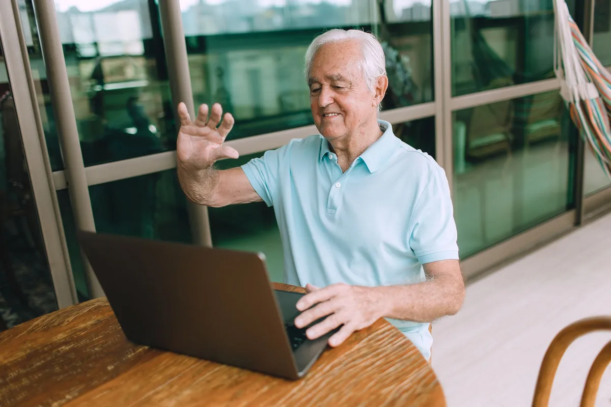 Homme âgé souriant lors d'un appel vidéo sur son ordinateur portable